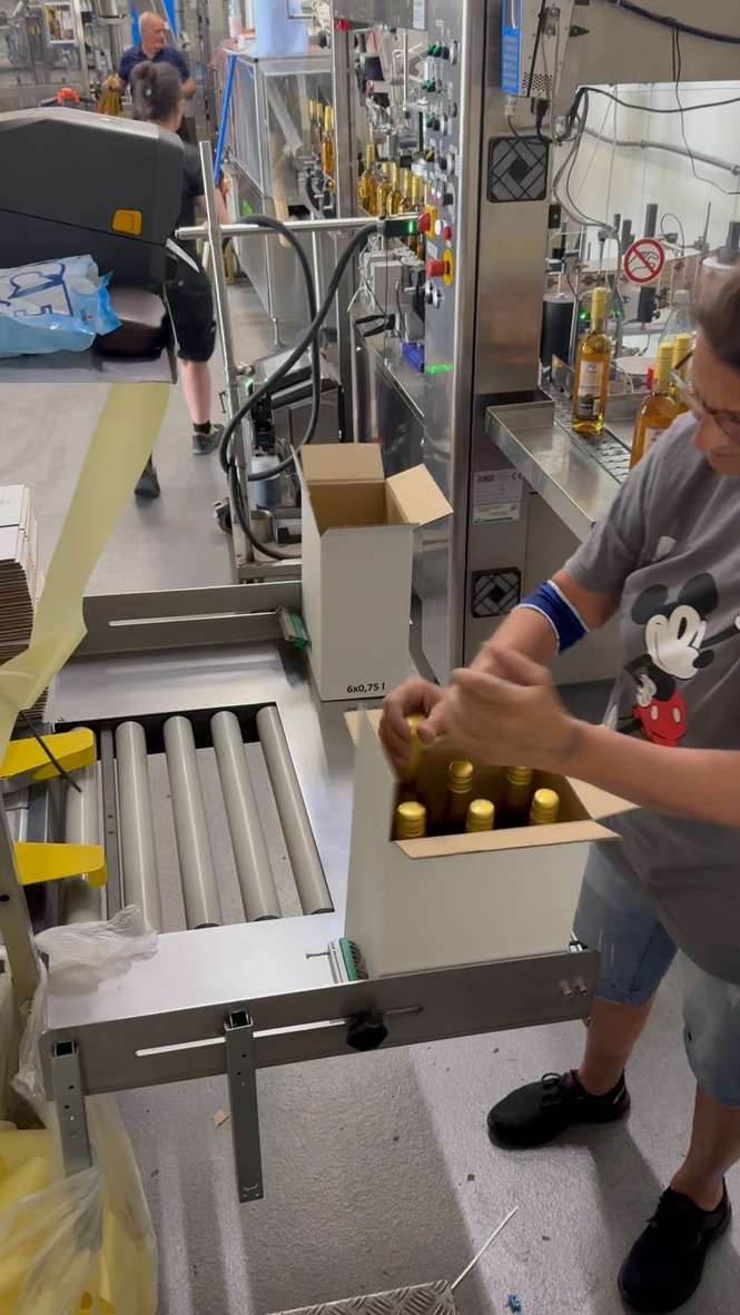 Worker packing SANZANA bottles into a cardboard box by hand